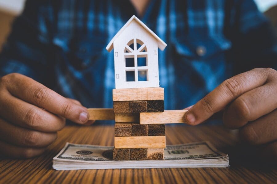 A tiny house atop a Jenga tower, with pieces being removed, representing risk weighted assets.