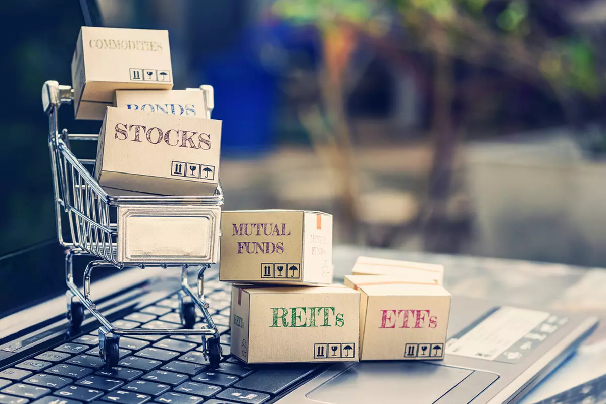 Cartons labeled with the names of financial instruments in a tiny shopping cart on top of a laptop keyboard.